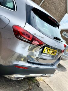 A rear view of a silver Mercedes-Benz GLA 200 parked on the side of a road. The car's license plate reads "LX70 GMW." The image captures the vehicle's tail lights and distinctive branding, with another car partially visible in the background.